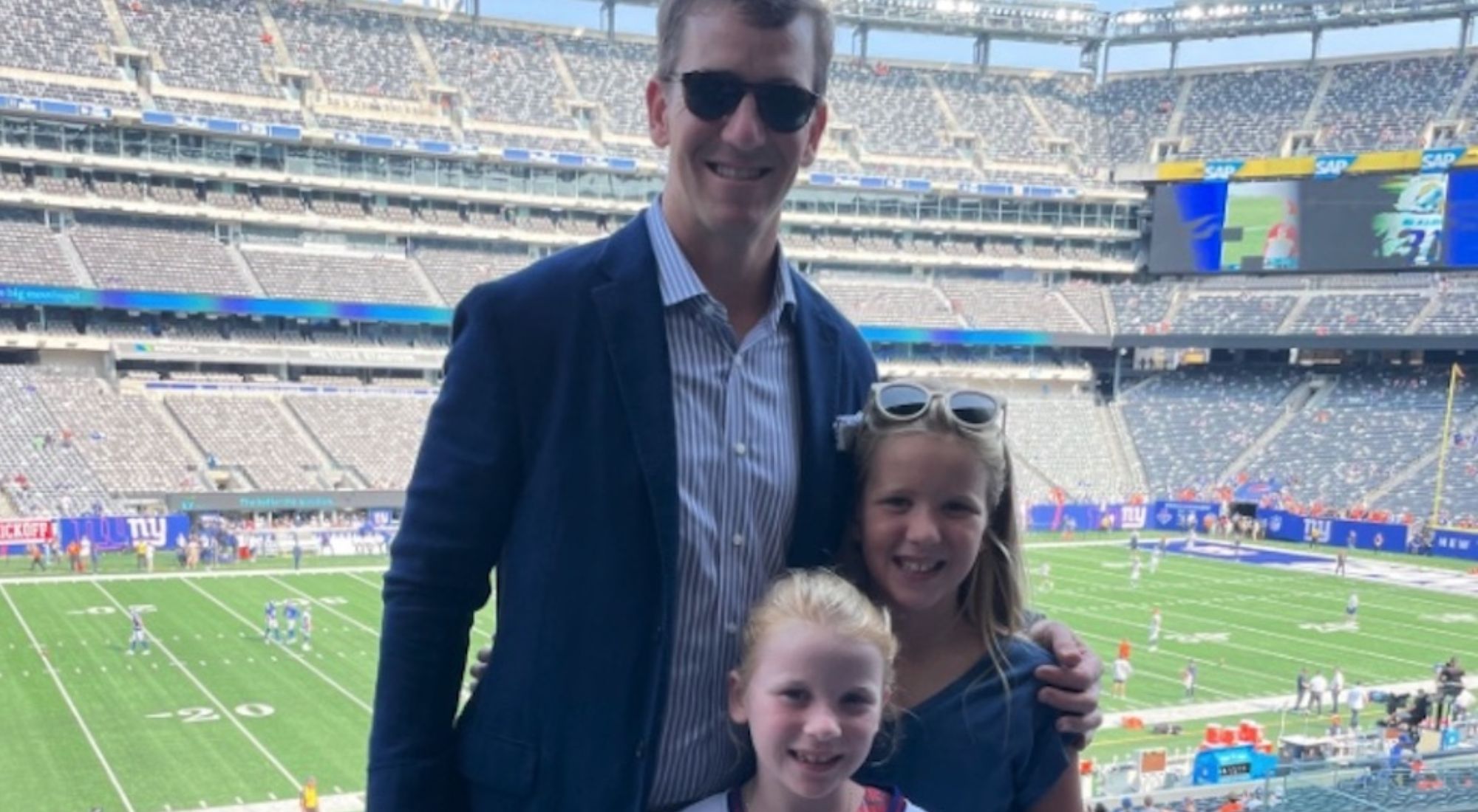 Eli Manning and two of his daughters at MetLife Stadium, smiling at the camera.