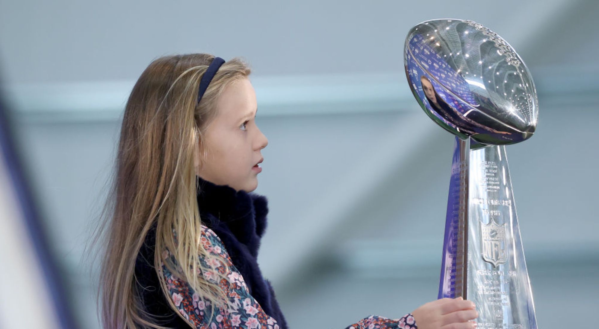 Eli Manning kid Lucy staring at a football trophy.