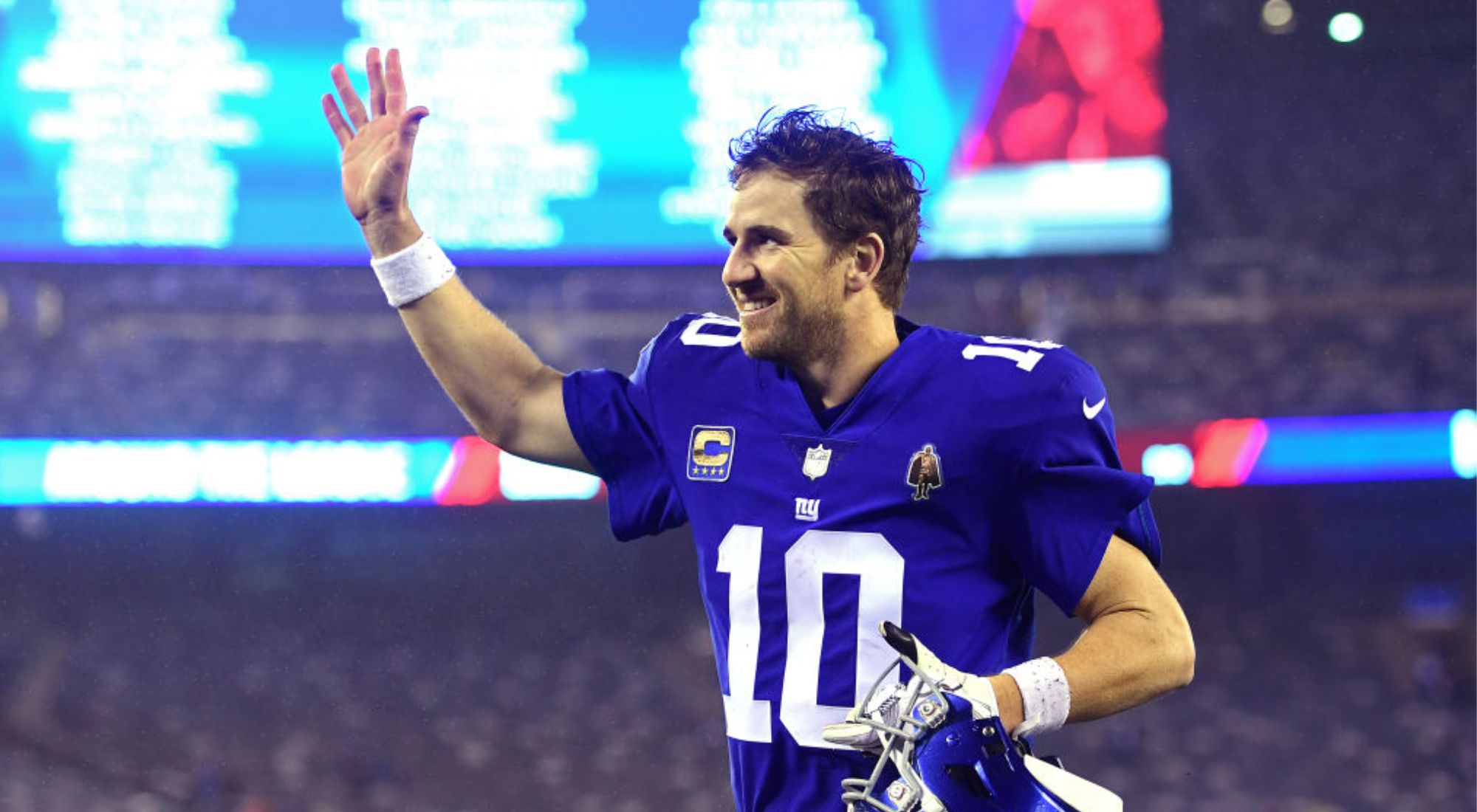 Eli Manning wearing New York Giants number 10 jersey waiving and smiling to fans.