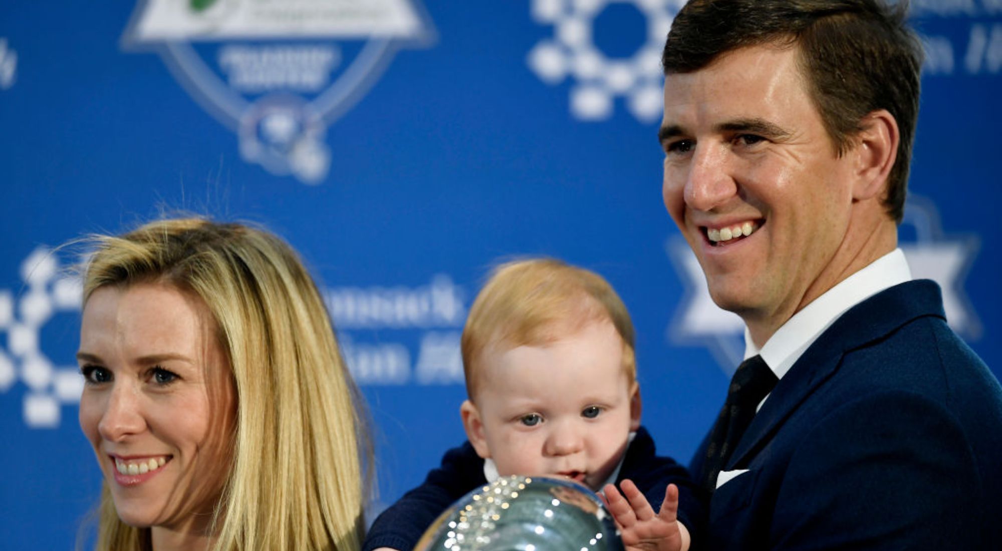 Eli Manning's child Charlie and his wife posing for cameras with a trophy.