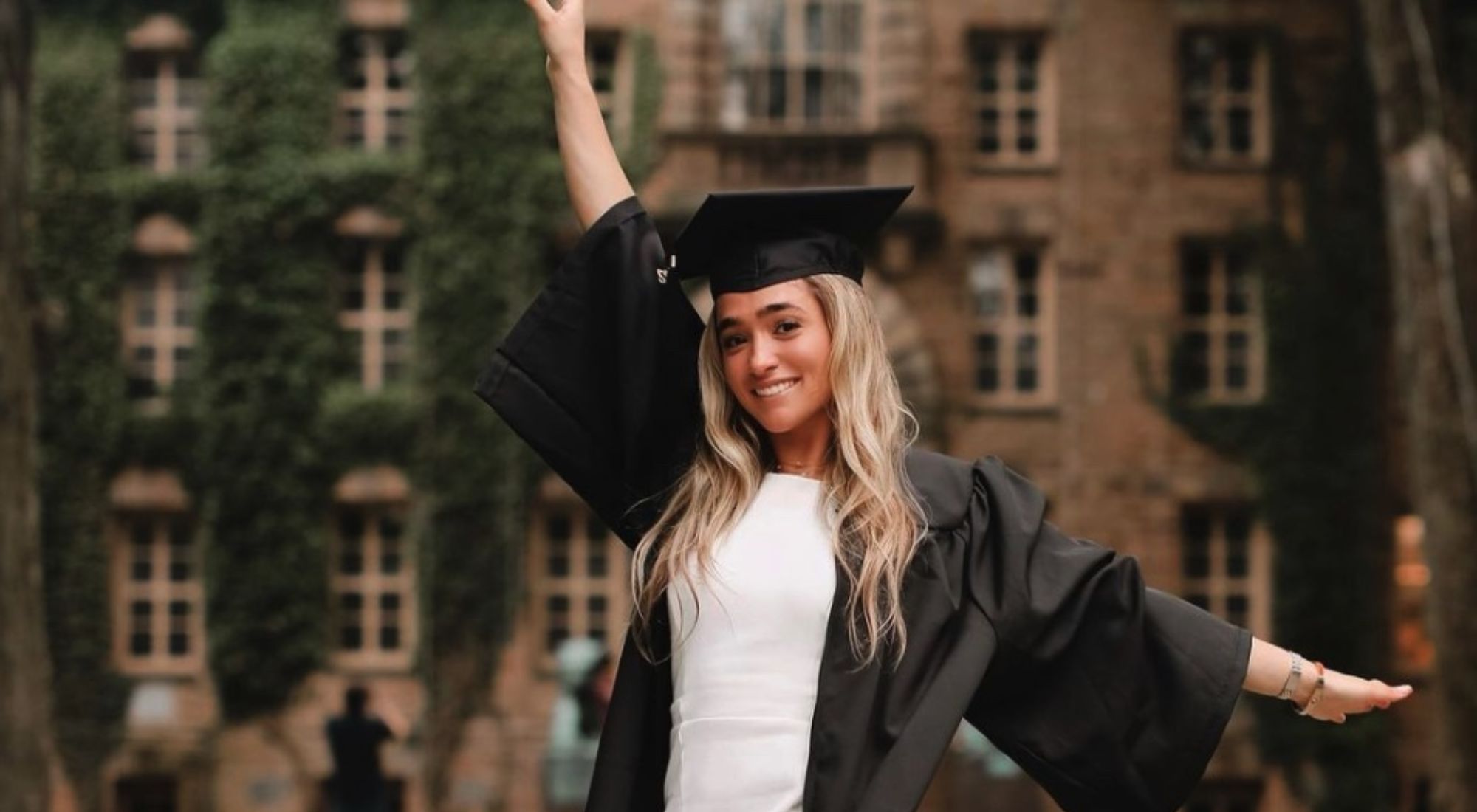 Amy Paternoster posing in her Princeton graduation cap and gown, with the school behind her.