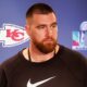 Travis Kelce speaking to reporters with Nike shirt on.