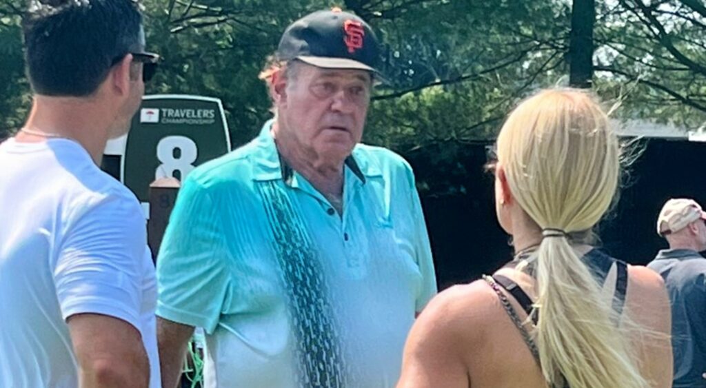 Chris Berman on golf course talking to woman.