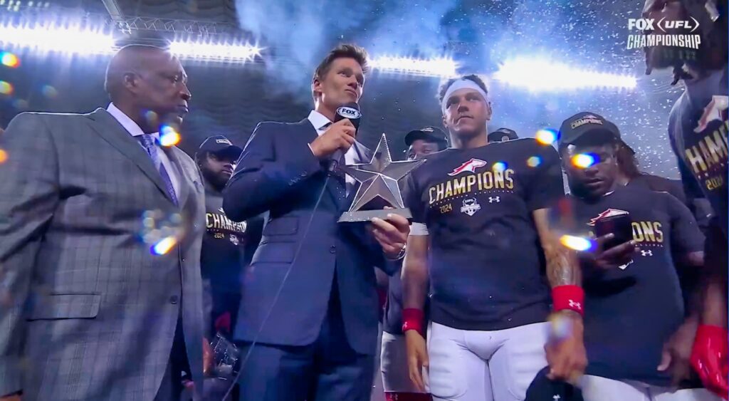 Tom Brady presents a trophy on the stage at the UFL Championship Game.