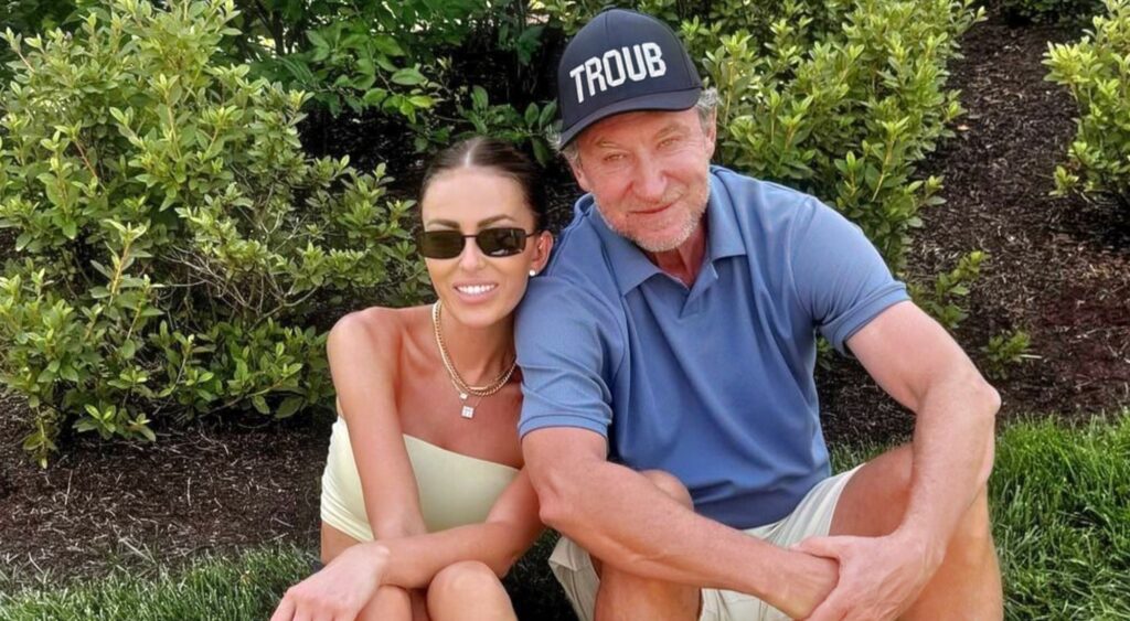 Wayne Gretzky and Paulina posing while seated on grass