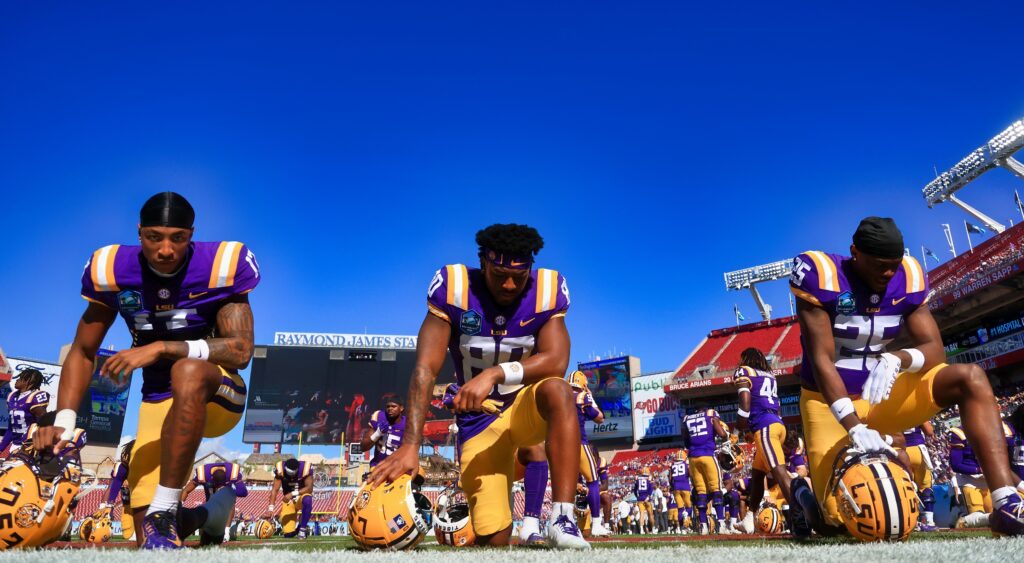 Chris Hilton Jr. #17, Gregory Clayton Jr. #80, and Javien Toviano #25 of the LSU Tigers on one knee on the field