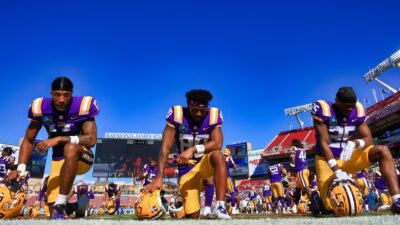 Chris Hilton Jr. #17, Gregory Clayton Jr. #80, and Javien Toviano #25 of the LSU Tigers on one knee on the field