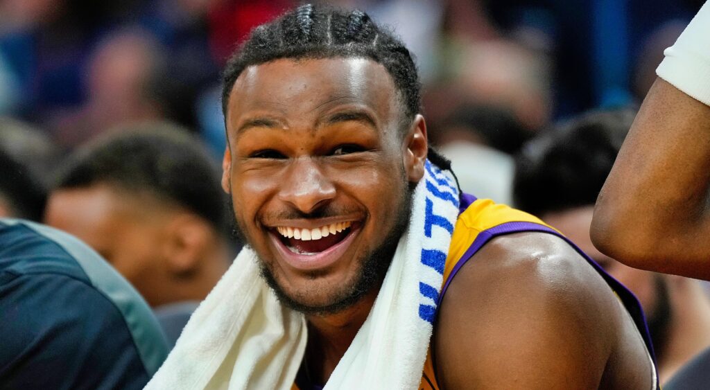 Bronny James laughs while sitting on the bench.