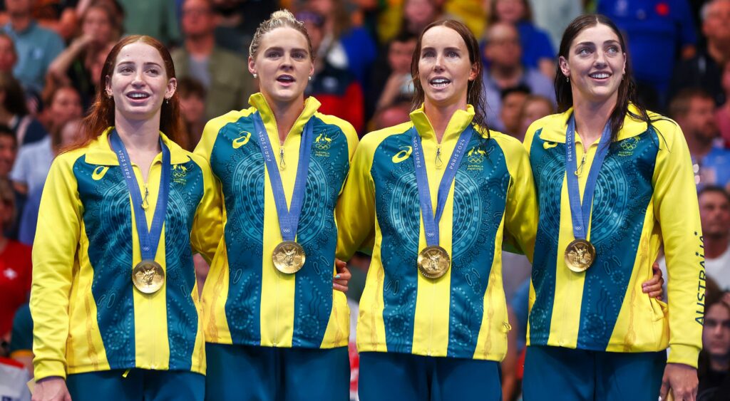 Australian women's swim team posing with medals. Announcer Bob Ballard was fired after making an inappropriate comment during their event.