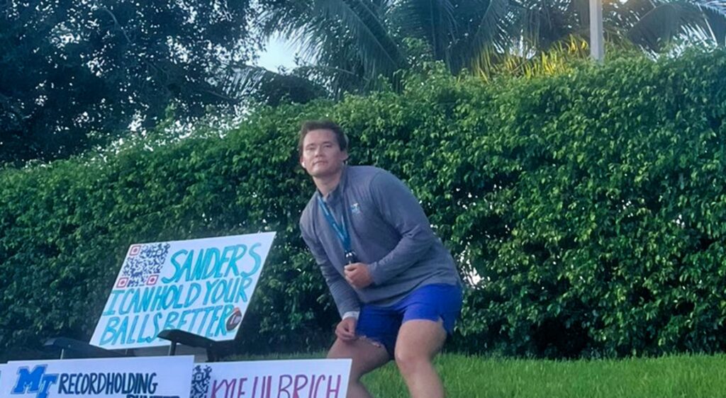 Kyle Ulbrich poses in front of his signs outside the Miami Dolphins practice facility.