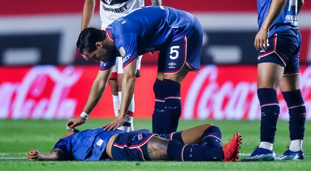 Juan Izquierdo lying on the field surrounded by teammates