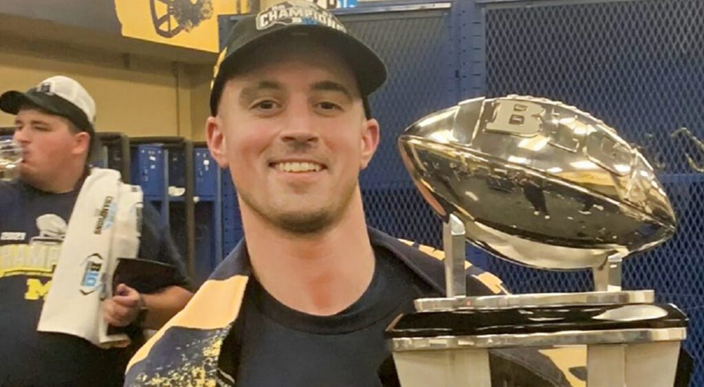 Connor Stalions posing in lokcer room with trophy