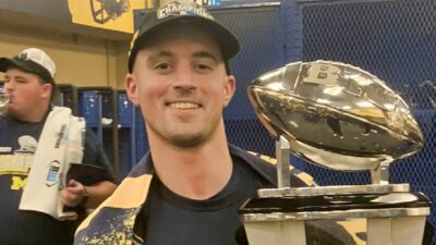 Connor Stalions posing in lokcer room with trophy