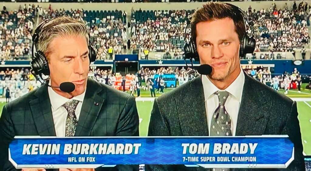 Kevin Burkhardt and Tom Brady speaking in broadcast booth.