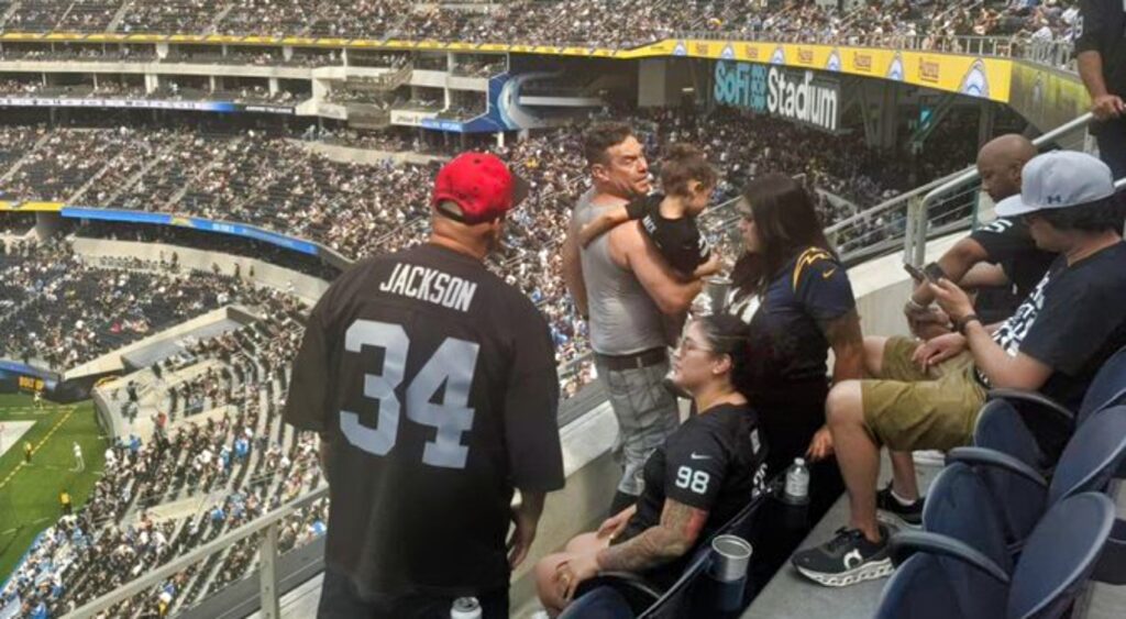 Raiders fan holding his daughter in the stands at SoFi Stadium.