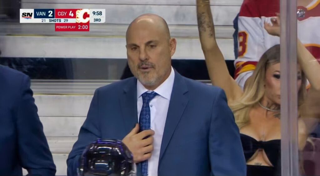 Vancouver Canucks coach Rick Tocchet and Calgary Flames fan behind the bench.