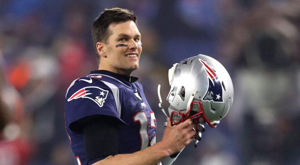 Tom Brady of the New England Patriots looks on holding his helmet 